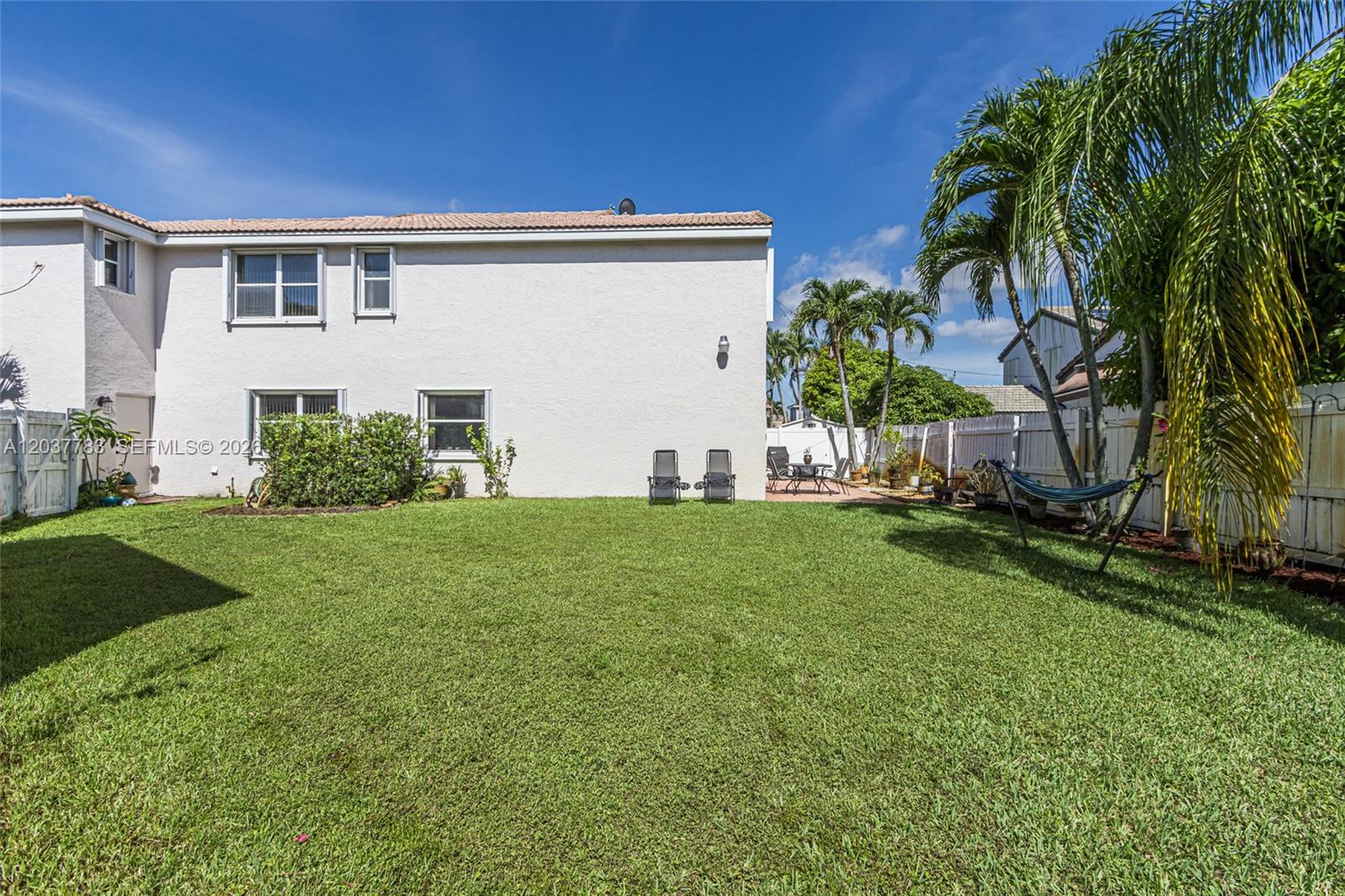 The backyard of a two-story house features a lawn, patio furniture, and palm trees — 17367 SW 20th Ct, Miramar FL 33029, MIRAMAR, FL