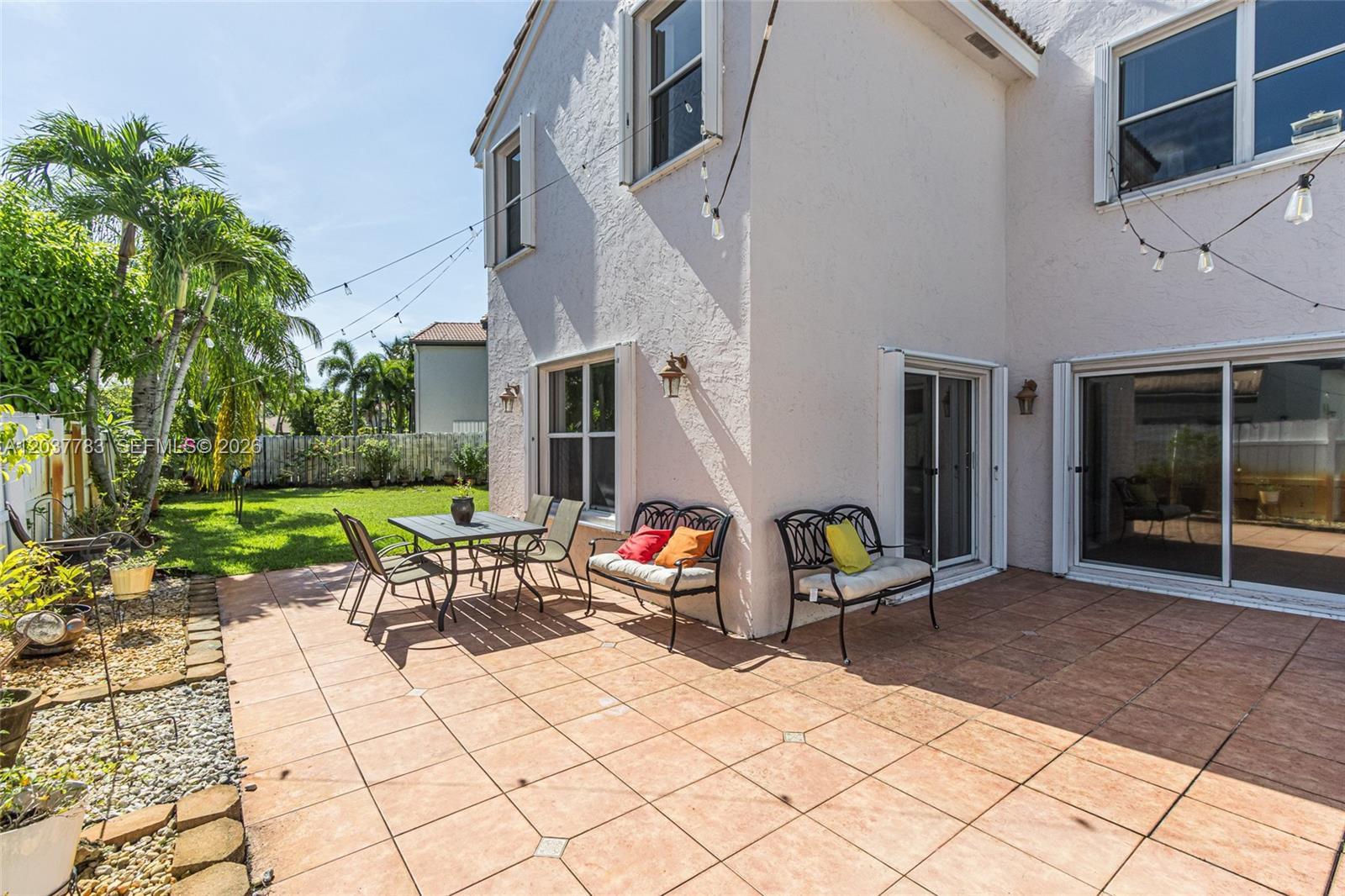 A tiled patio features outdoor furniture and string lights against the side of a house — 17367 SW 20th Ct, Miramar FL 33029, MIRAMAR, FL