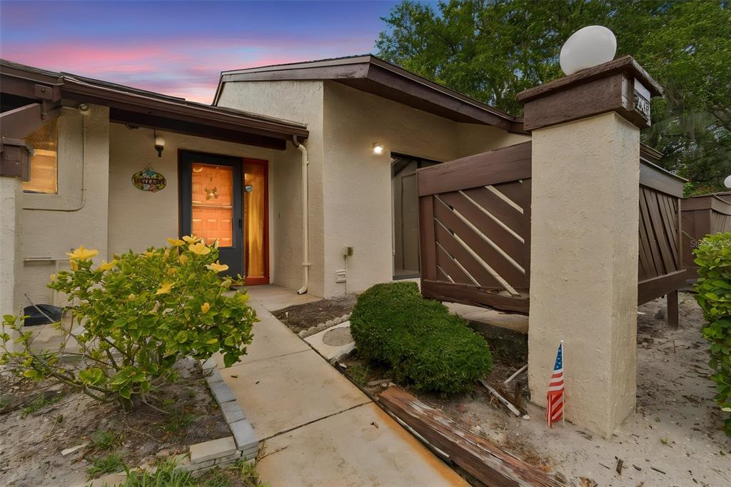 An exterior view of a house entrance with a concrete walkway, landscaping, and wooden fencing — 2903 FIG COURT, PALM HARBOR, FL