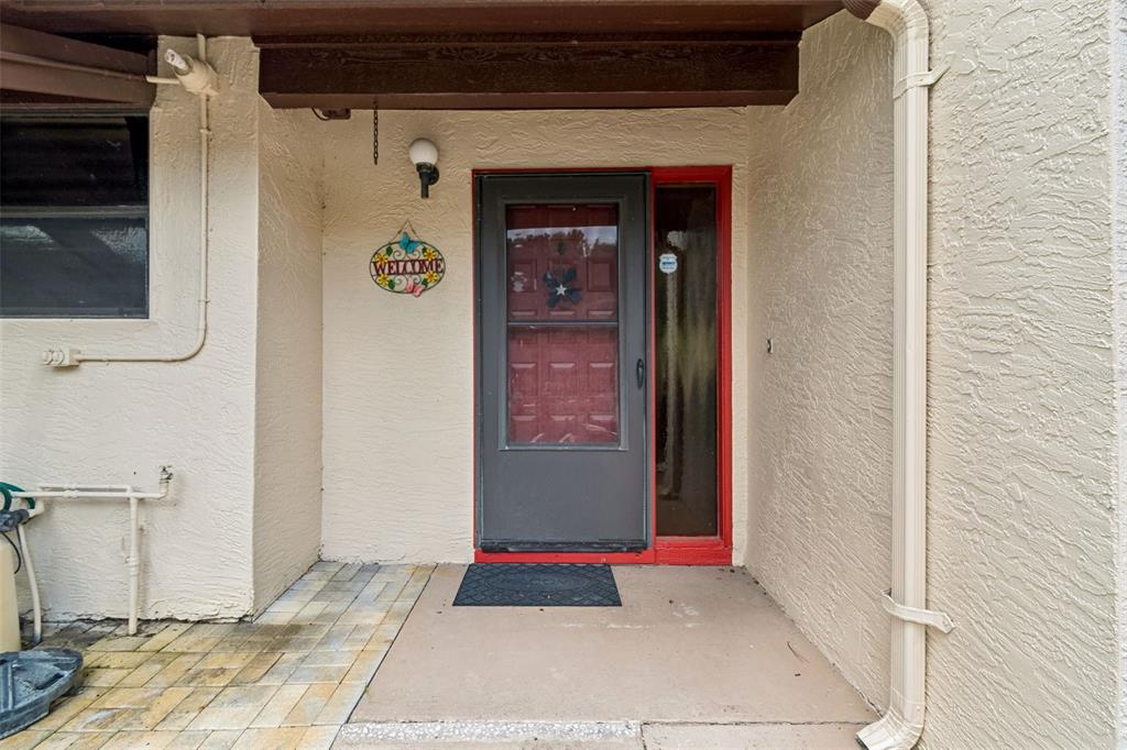 A covered entryway features a red front door with a storm door and a welcome sign — 2903 FIG COURT, PALM HARBOR, FL
