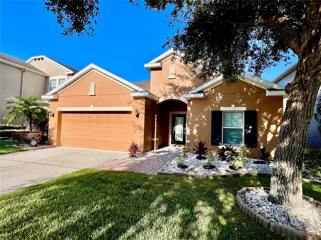 A single-story house with a tan stucco exterior, a two-car garage, and a paved walkway — 9606 OAK GLADE AVENUE, TAMPA, FL