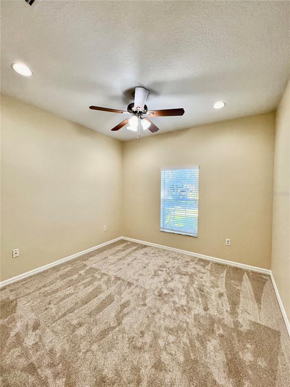 An empty bedroom features beige walls, tan carpet, a ceiling fan, and a single window — 9606 OAK GLADE AVENUE, TAMPA, FL