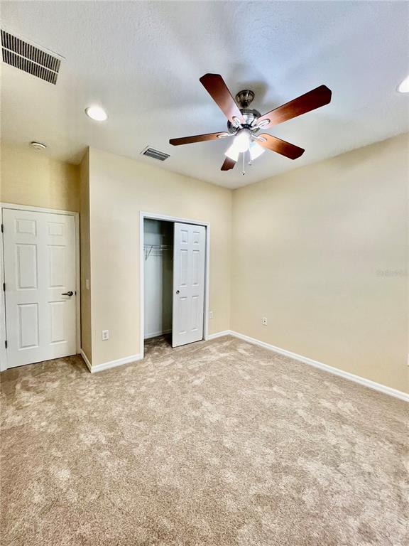 An empty bedroom features beige carpet, light-colored walls, a ceiling fan, and a closet — 9606 OAK GLADE AVENUE, TAMPA, FL