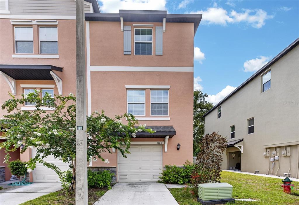 A three-story peach-colored townhouse with a white garage door and a small front yard — 4424 TUSCAN LOON DRIVE, TAMPA, FL
