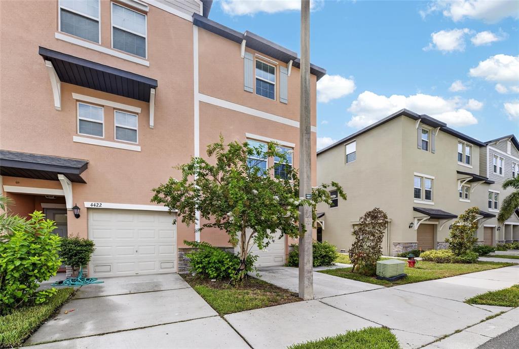 A multi-story townhouse with a peach-colored exterior, a garage, and a small front yard — 4424 TUSCAN LOON DRIVE, TAMPA, FL