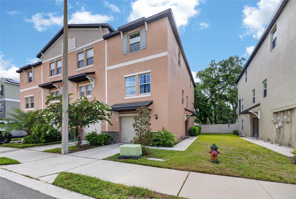 A three-story peach-colored townhouse with a garage and a side yard with a fire hydrant — 4424 TUSCAN LOON DRIVE, TAMPA, FL