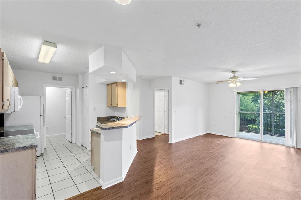 A kitchen with tile floors and a breakfast bar opens into a wood-floored living area — 12602 CREST SPRINGS LANE UNIT 1331, ORLANDO, FL