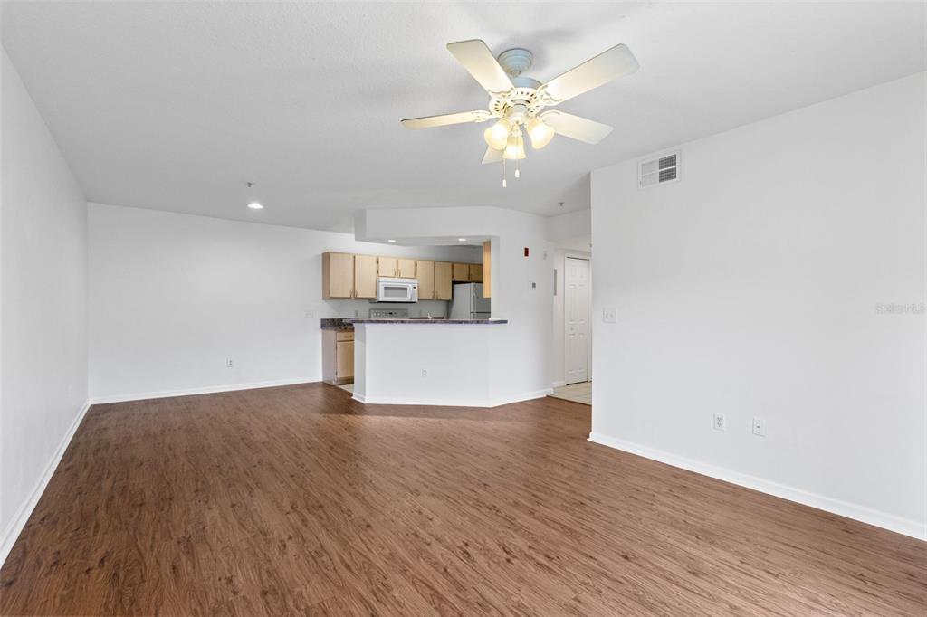 An open-concept living area features wood-look flooring, a ceiling fan, and a kitchen with cabinets — 12602 CREST SPRINGS LANE UNIT 1331, ORLANDO, FL