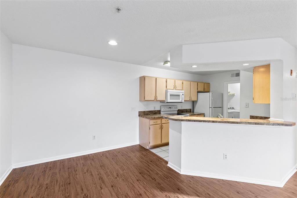 A kitchen with light wood cabinets, laminate countertops, and white appliances overlooks a dining area — 12602 CREST SPRINGS LANE UNIT 1331, ORLANDO, FL