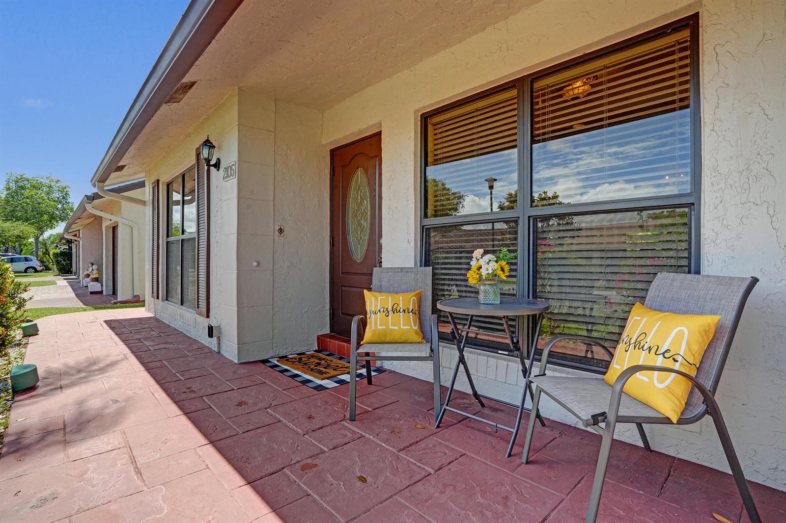A covered front porch features red stone-look pavers, two chairs with yellow pillows, and a table — 2105 SW 17th Circle, Deerfield Beach FL 33442, DEERFIELD BEACH, FL