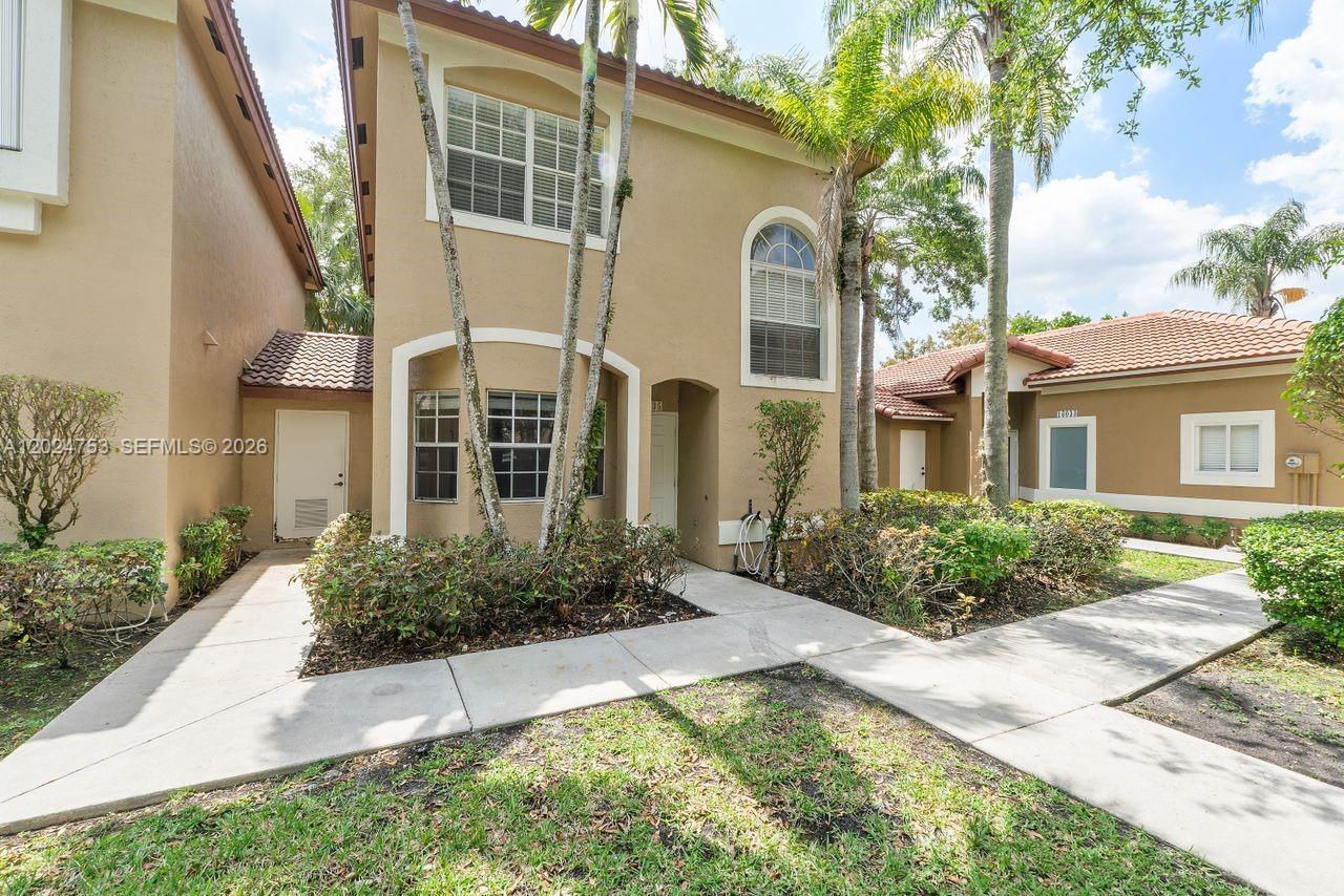 A two-story tan stucco townhouse features a front walkway, arched entryway, and palm trees — 16035 Emerald Cove Rd, Weston FL 33331, WESTON, FL