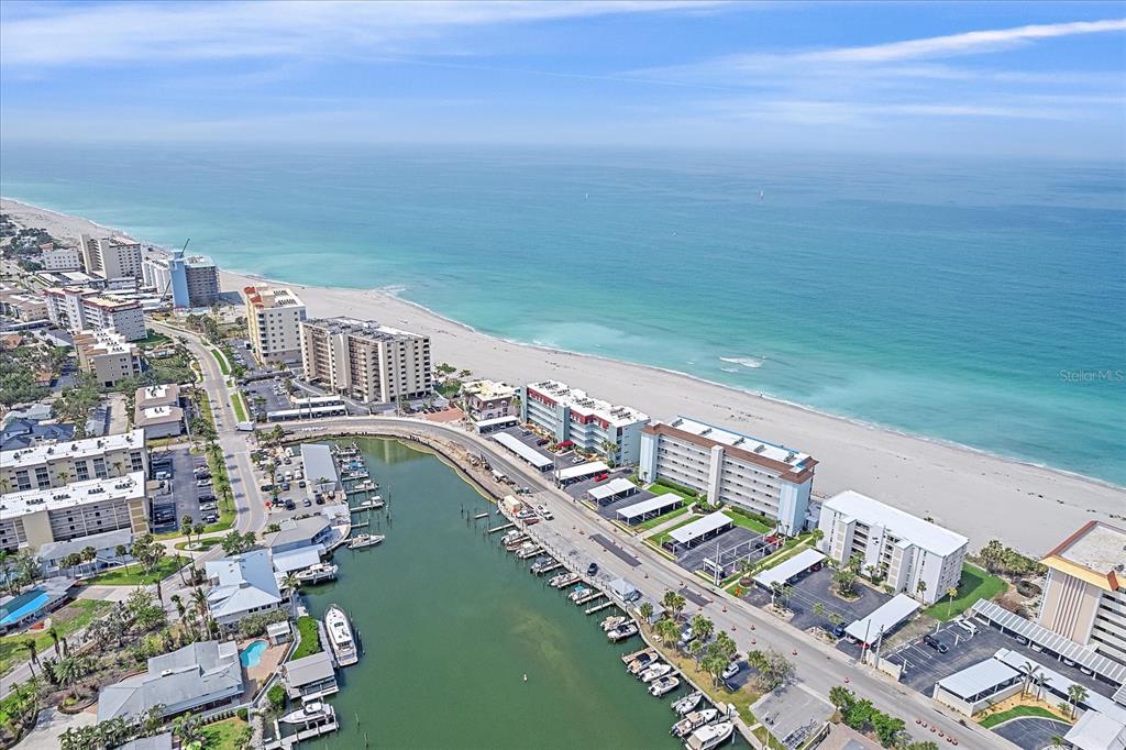 An aerial view shows a coastal beach, multi-story residential buildings, and a boat-filled marina — 950 TARPON CENTER DRIVE UNIT 504, VENICE, FL