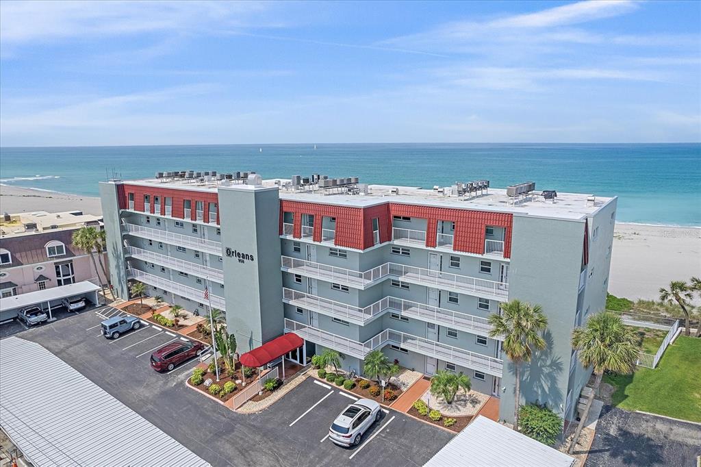 An aerial view shows a multi-story apartment building with a red roof near the ocean — 950 TARPON CENTER DRIVE UNIT 504, VENICE, FL