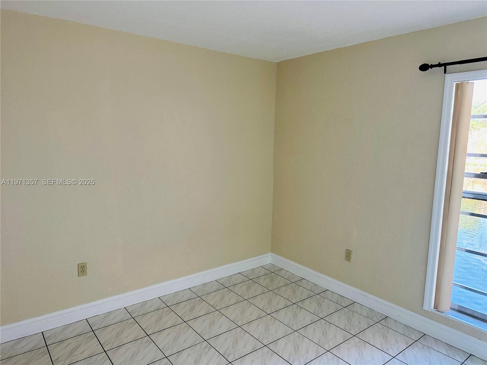 An empty room features beige walls, white baseboards, tiled flooring, and a sliding glass door — 4705 NW 7th St # 7, Miami FL 33126, MIAMI, FL
