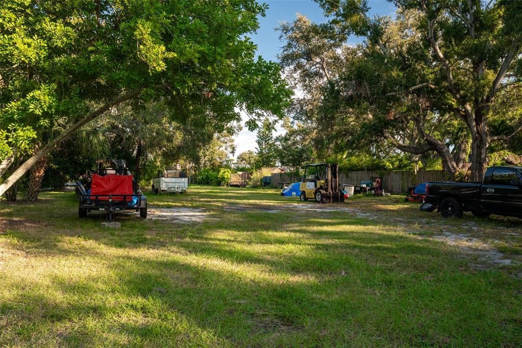 A grassy lot features a trailer, a forklift, and a black pickup truck under trees — 6027 98TH WAY N, ST PETERSBURG, FL