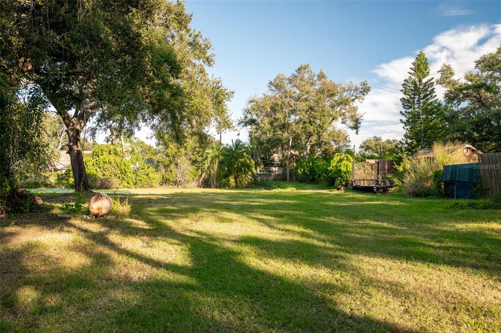 A large, grassy backyard features mature trees, a small trailer, and a covered structure — 6027 98TH WAY N, ST PETERSBURG, FL