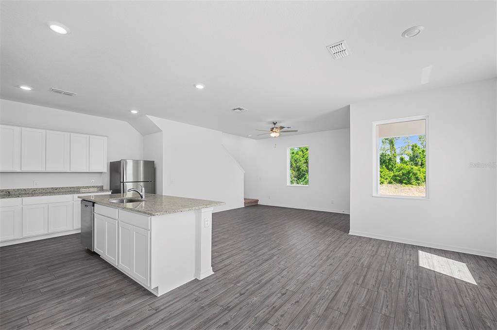 A kitchen with white cabinets and a granite island opens to a spacious living area — 552 BAY LEAF DRIVE, POINCIANA, FL