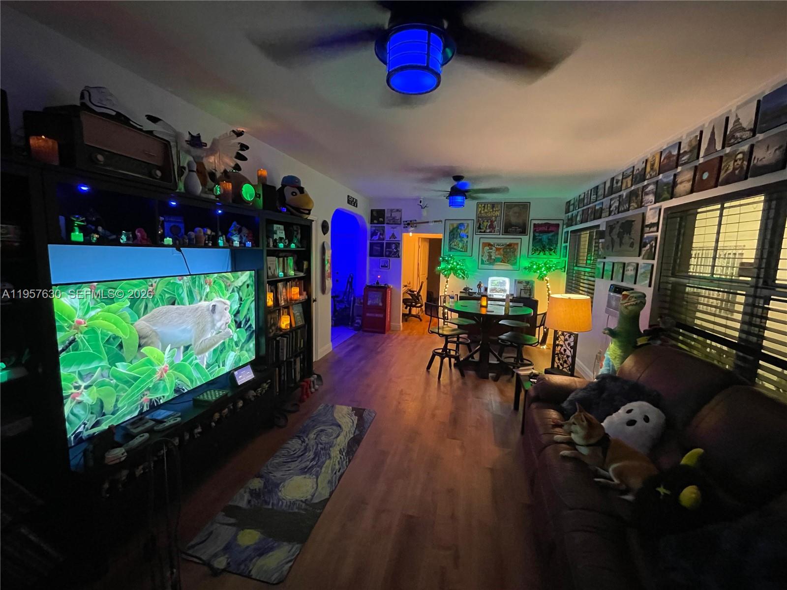 A living room features a large television, wooden flooring, ceiling fans, and a leather sofa — 2463 Pine Tree Dr # 4, Miami Beach FL 33140, MIAMI BEACH, FL