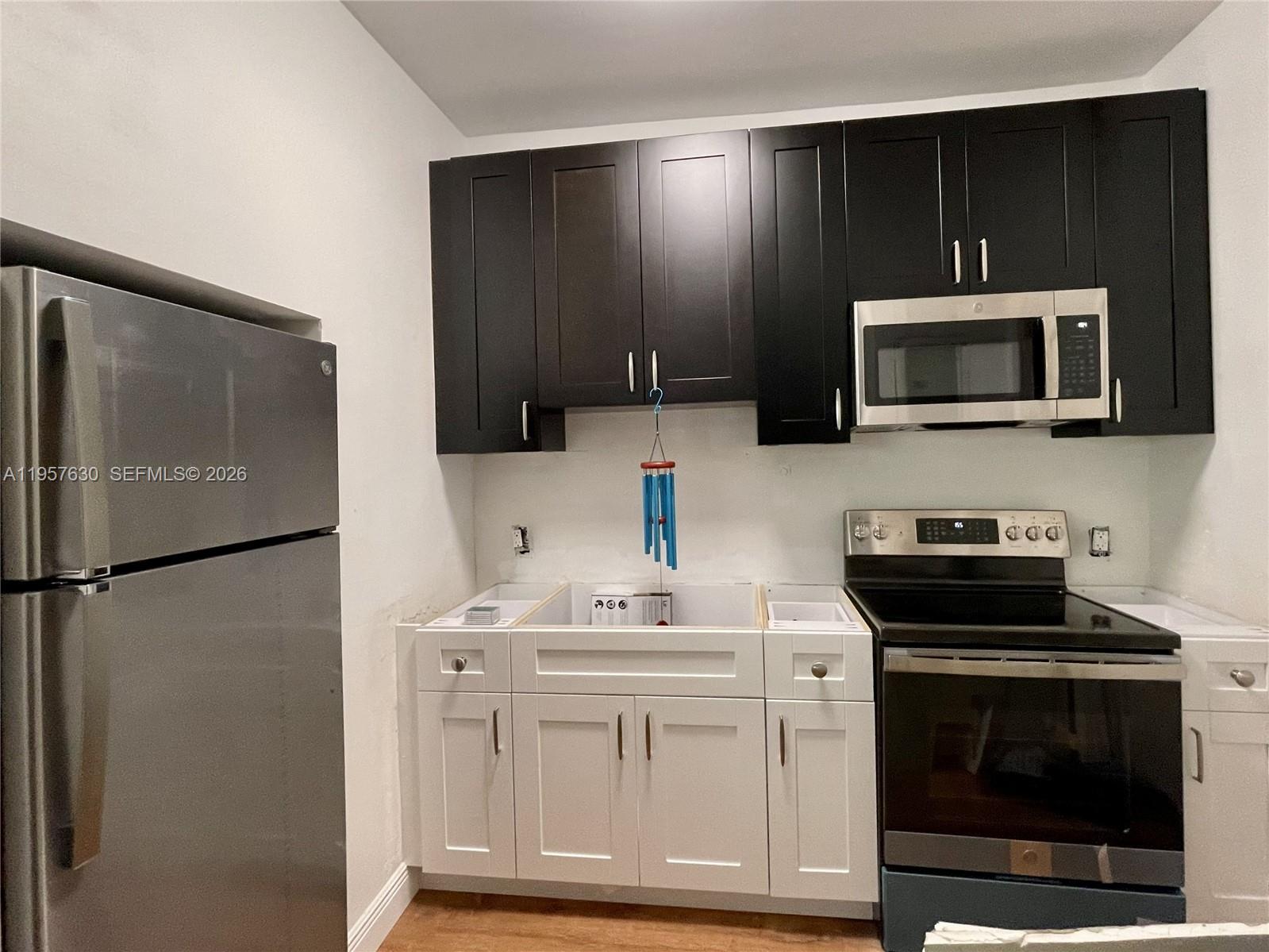 A kitchen features dark upper cabinets, white lower cabinets, a stainless steel refrigerator, and stove — 2463 Pine Tree Dr # 4, Miami Beach FL 33140, MIAMI BEACH, FL
