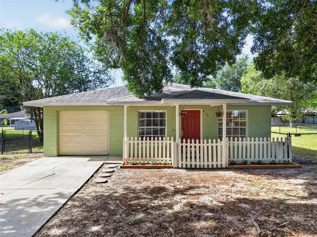 A light green, single-story concrete block house features a red door and white picket fence — 610 PALMETTO DRIVE, MASCOTTE, FL
