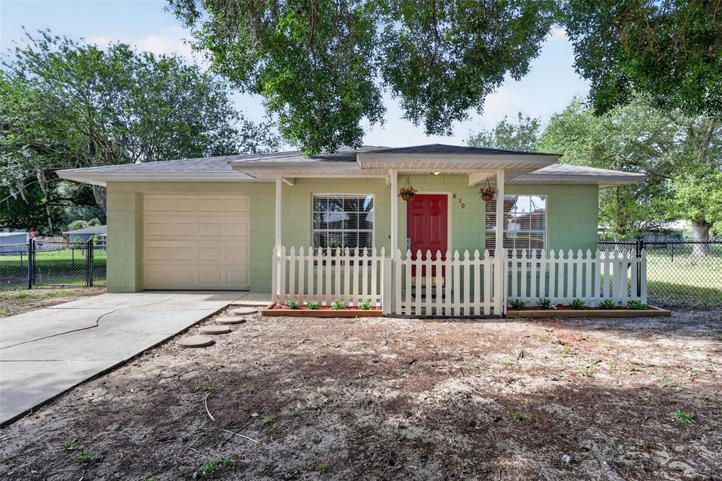 A single-story house with light green concrete block walls, a red door, and a white fence — 610 PALMETTO DRIVE, MASCOTTE, FL