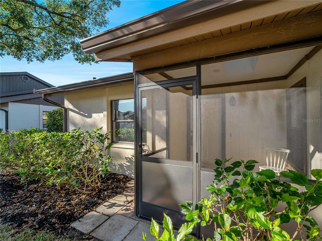 A screened-in porch with a white chair sits beside a house with tan siding — 365 OAK HILL WAY UNIT 32, SARASOTA, FL