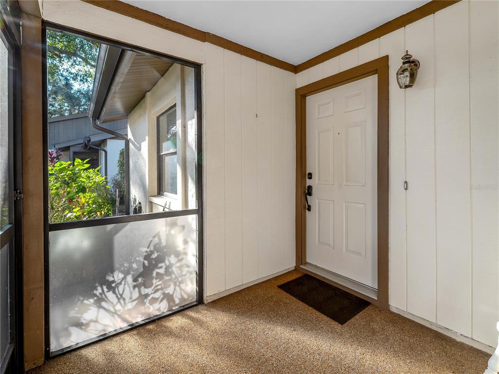 A covered entryway features a white front door, textured flooring, and a large screened window — 365 OAK HILL WAY UNIT 32, SARASOTA, FL