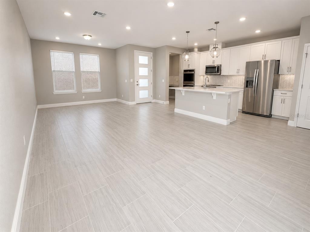 An open-concept kitchen and living area featuring light wood-look tile flooring and white cabinetry — 7248 CARRICKBEND LANE, ORLANDO, FL