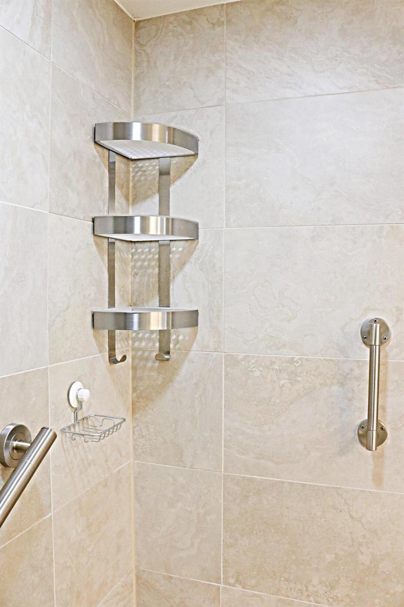 A shower corner features a three-tier metal shelf, a grab bar, and beige tiled walls — 230 NE 26th Avenue # 1070, Boynton Beach FL 33435, BOYNTON BEACH, FL