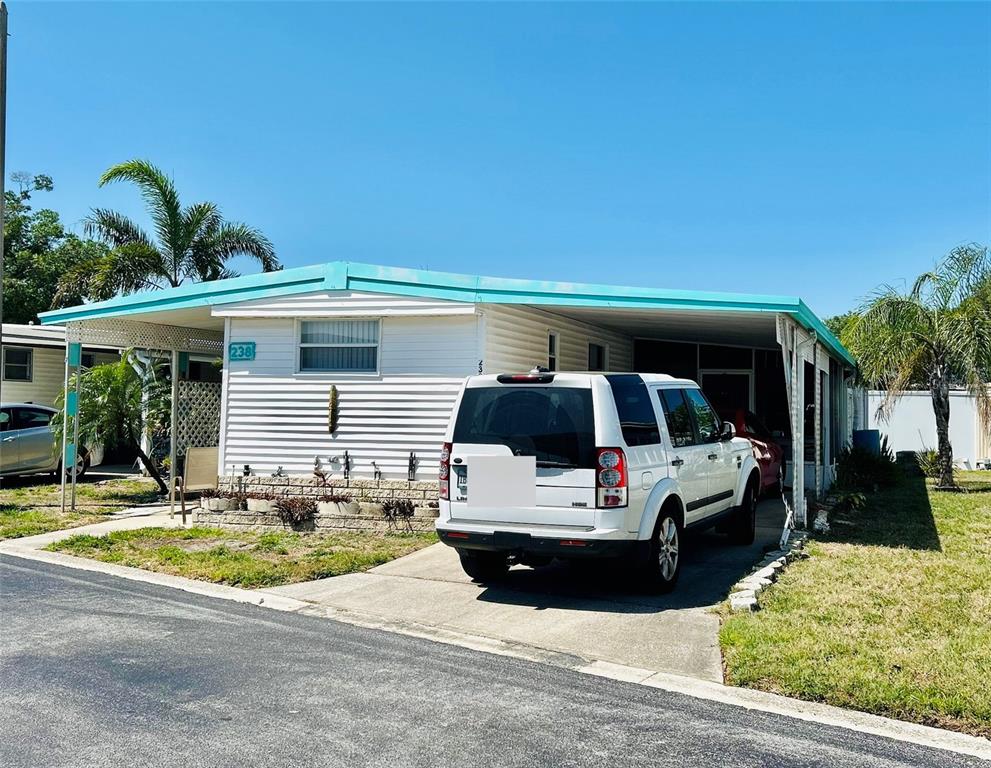 A white mobile home with a turquoise roof trim and a carport sits on a lot — 9790 66TH STREET N UNIT 238, PINELLAS PARK, FL
