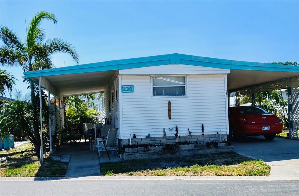 A white mobile home with a teal roof, a carport, and a red car parked outside — 9790 66TH STREET N UNIT 238, PINELLAS PARK, FL