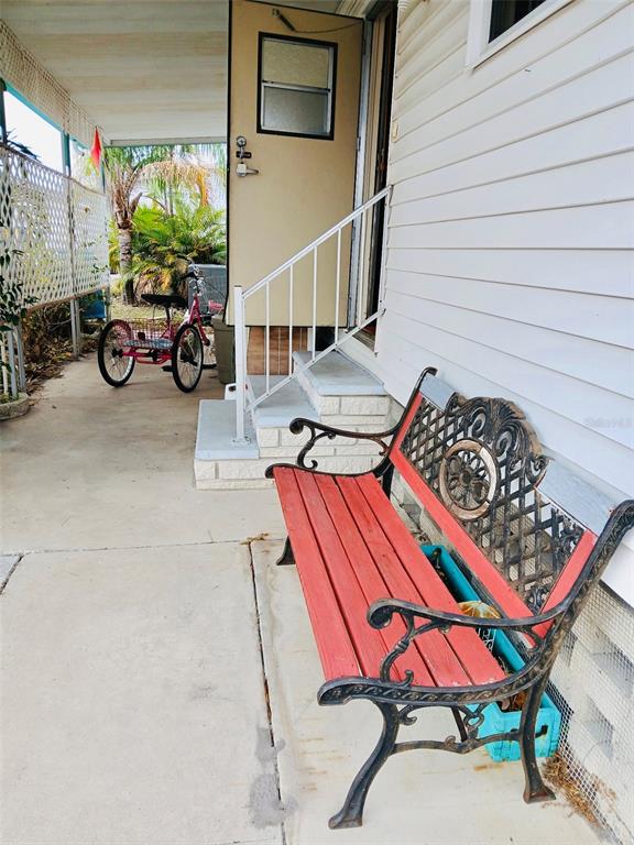 A red and black bench sits on a concrete porch next to a tricycle — 9790 66TH STREET N UNIT 238, PINELLAS PARK, FL