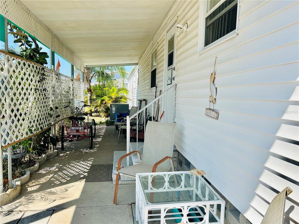 A covered concrete porch features a white lattice wall, a tricycle, and outdoor patio furniture — 9790 66TH STREET N UNIT 238, PINELLAS PARK, FL