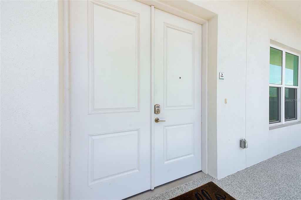 A white double front door with a smart lock and a small window nearby — 400 150TH AVENUE UNIT 504, MADEIRA BEACH, FL