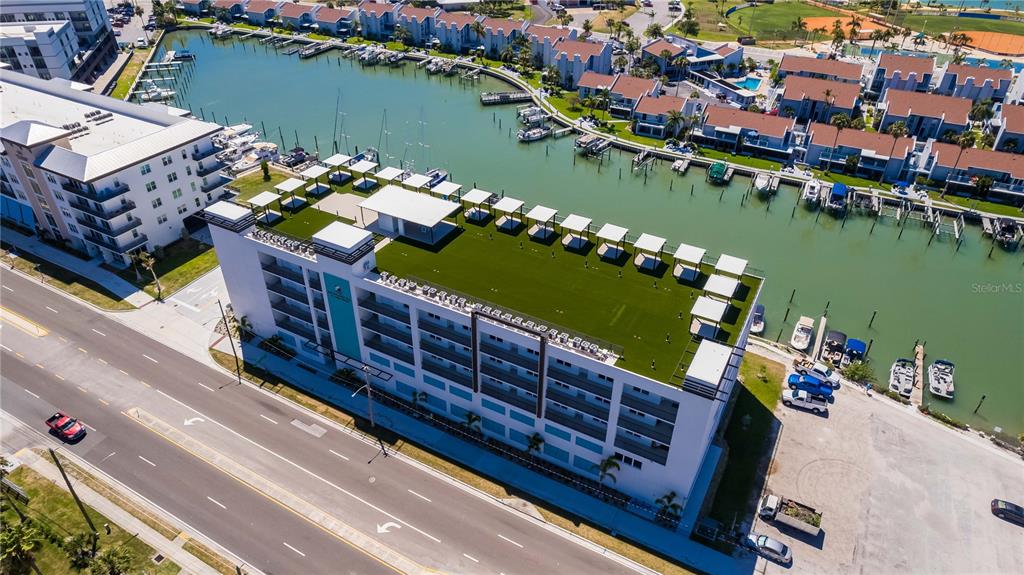 An aerial view shows a multi-story apartment building with a rooftop terrace beside a canal — 400 150TH AVENUE UNIT 504, MADEIRA BEACH, FL