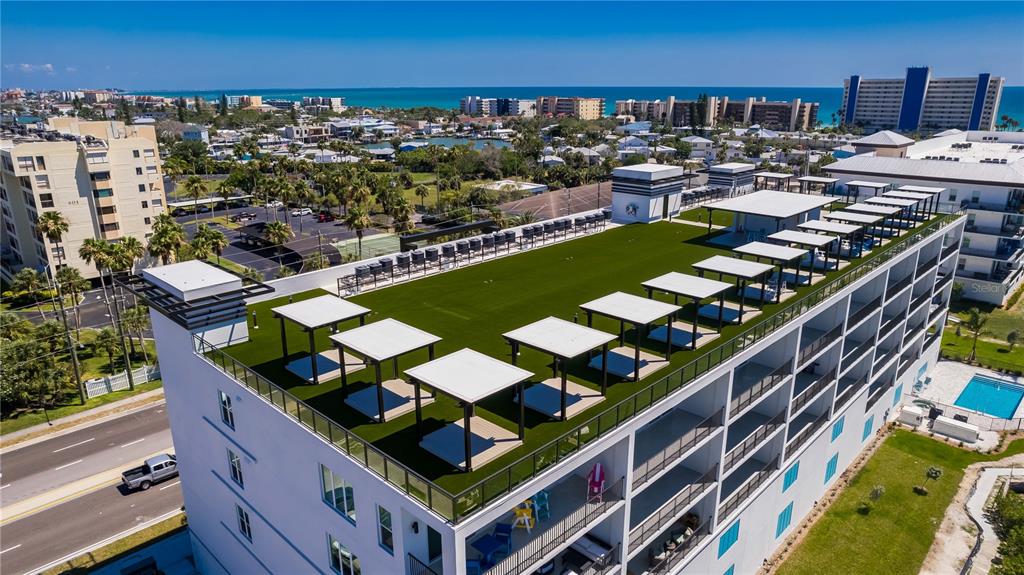 An aerial view of a building rooftop featuring artificial turf, multiple cabanas, and ocean views — 400 150TH AVENUE UNIT 504, MADEIRA BEACH, FL