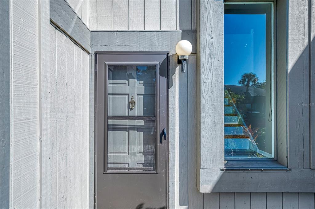 A brown storm door and a tall vertical window are set into a gray-painted exterior wall — 984 N BENEVA ROAD UNIT T7, SARASOTA, FL