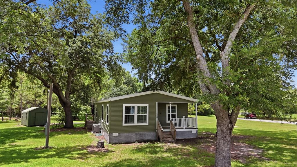 A green single-story house with a front porch sits on a grassy lot with trees — 7239 ROOKS DRIVE, WESLEY CHAPEL, FL