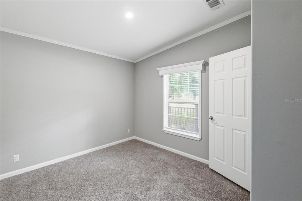 A bedroom with gray walls, gray carpet, a single window, and a white door — 7239 ROOKS DRIVE, WESLEY CHAPEL, FL