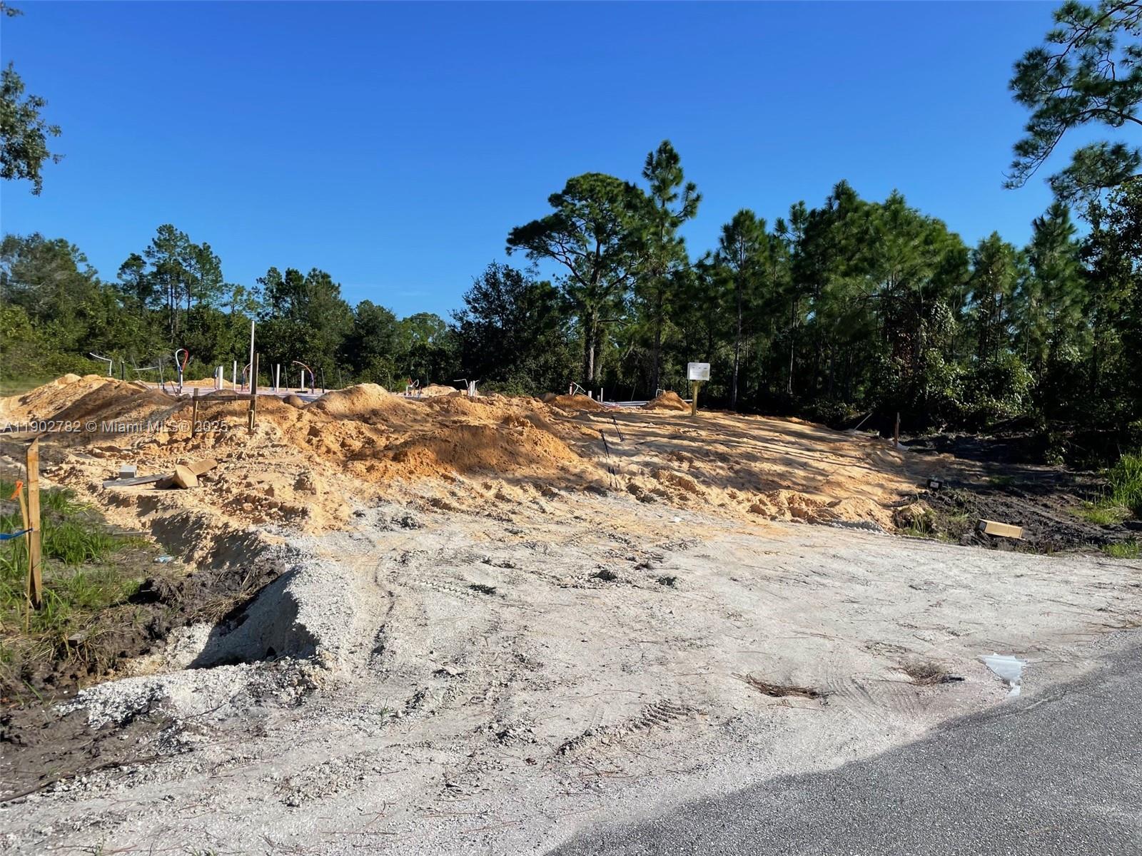 A dirt lot under construction features a concrete foundation and plumbing pipes amidst pine trees — 8030 SUN N LAKES, Sebring FL 33872, SEBRING, FL