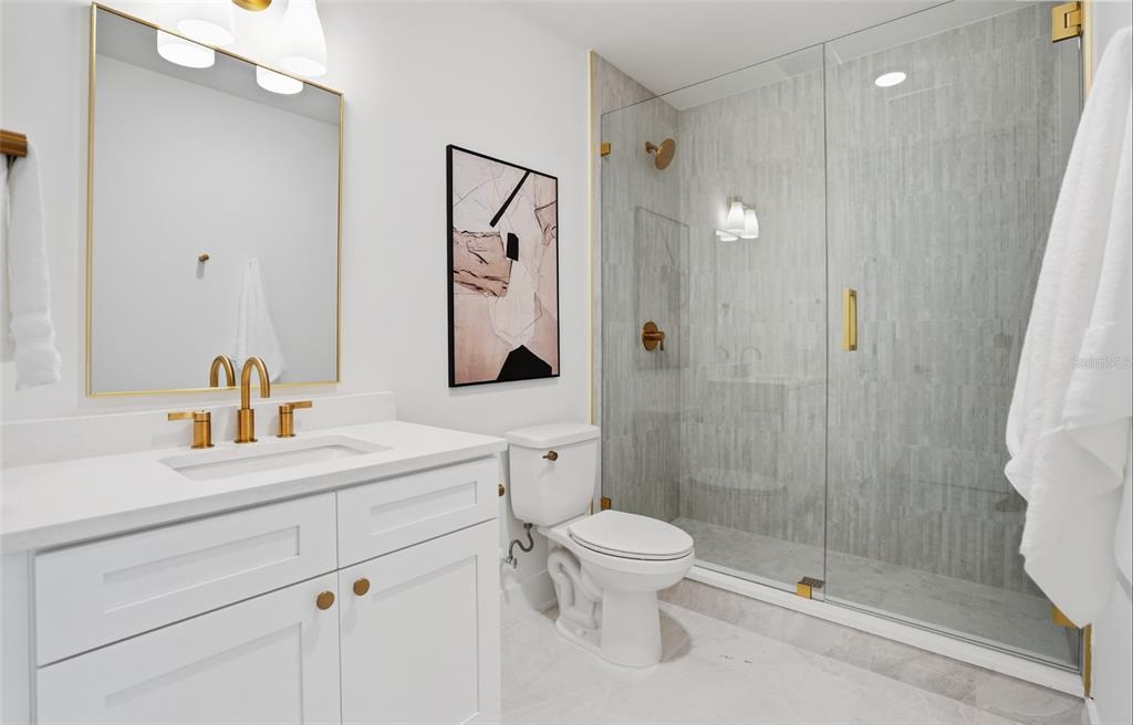 A modern bathroom features a white vanity, gold fixtures, a toilet, and a glass-enclosed shower — 3002 W PLATT UNIT 3, TAMPA, FL