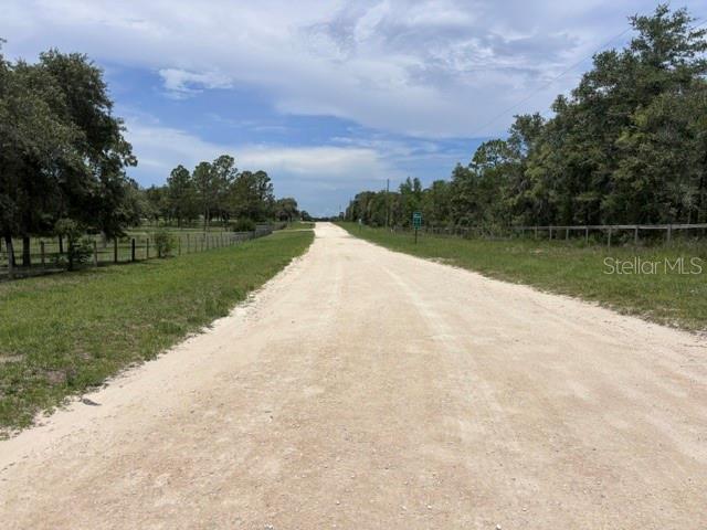 A dirt road stretches into the distance between grassy fields and wooded areas — SE 16 LANE, MORRISTON, FL