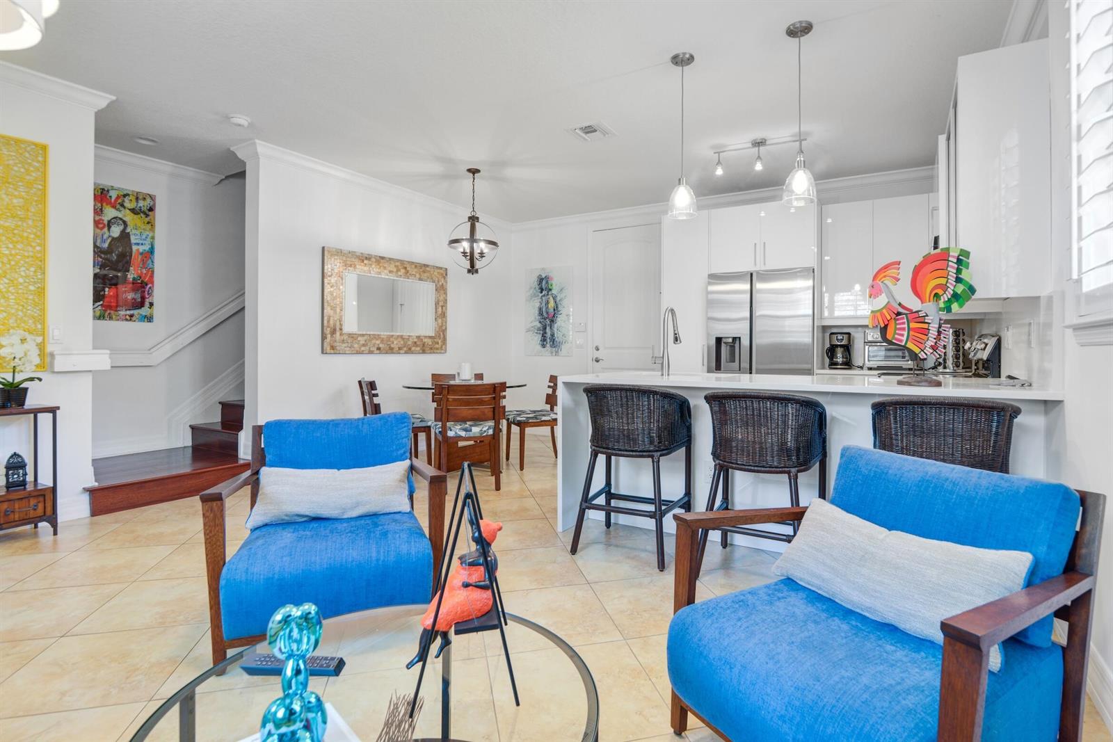 A bright living room and kitchen area features blue armchairs, a dining table, and stools — 861 S Ocean Boulevard, Pompano Beach FL 33062, POMPANO BEACH, FL