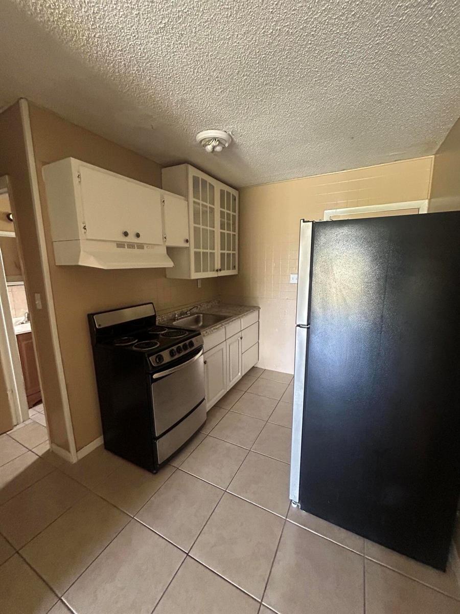 A kitchen features a black stove, a black refrigerator, white cabinets, and tiled flooring — 8657 64th Court, Vero Beach FL 32967, VERO BEACH, FL