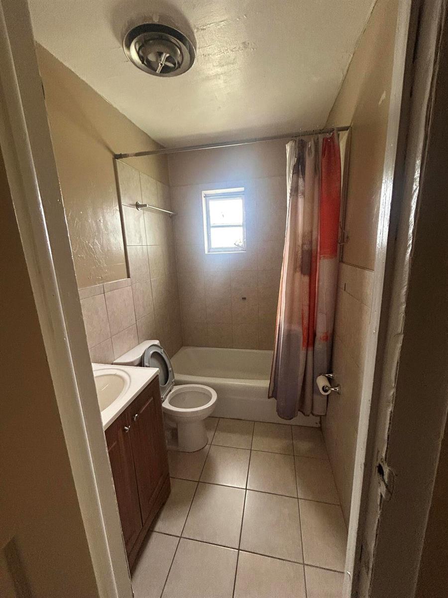 A small bathroom features a vanity, a toilet, and a shower-tub combination with tiled walls — 8657 64th Court, Vero Beach FL 32967, VERO BEACH, FL