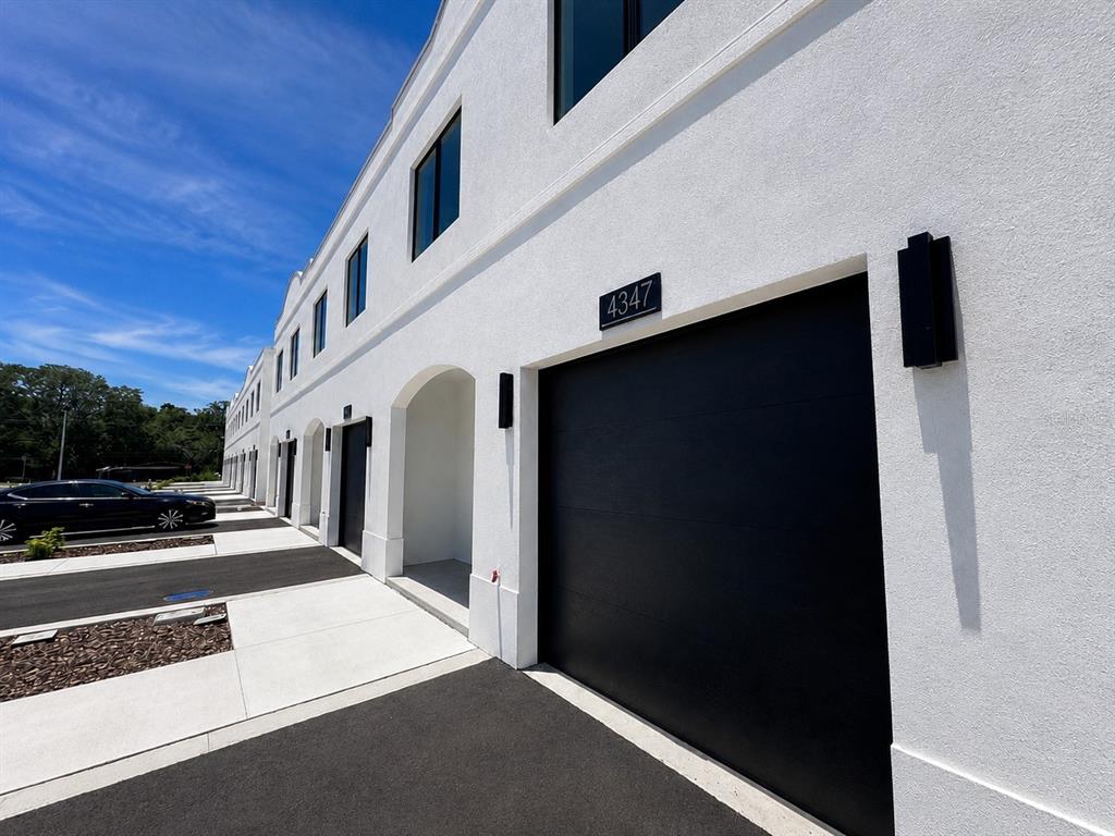 A row of modern white townhomes features black garage doors and matching exterior light fixtures — 4347 CAMBIO GARDENS COURT, TAMPA, FL