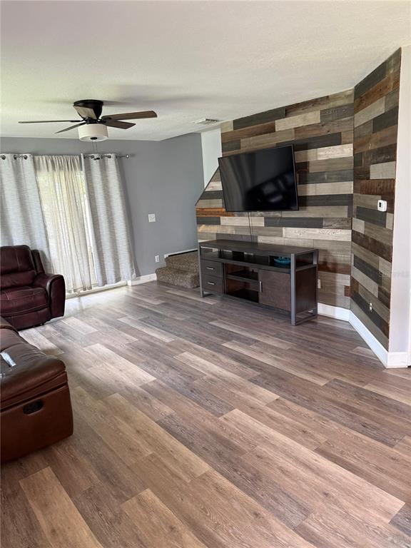 A living room features wood-look flooring, a wood-paneled accent wall, and a television console — 2235 FLUORSHIRE DRIVE, BRANDON, FL