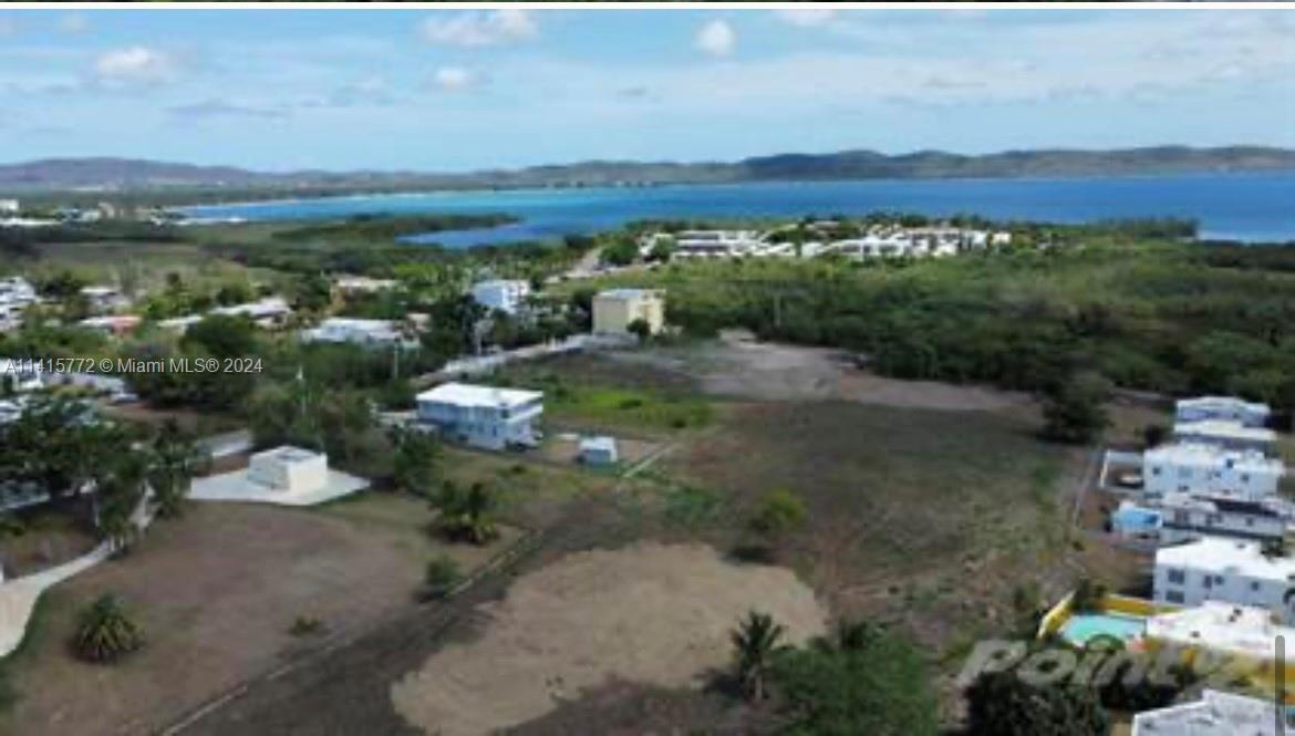 An aerial view shows a coastal landscape with scattered houses, open land, and the ocean — Carretera 307 KM 7, PR 00623, PR