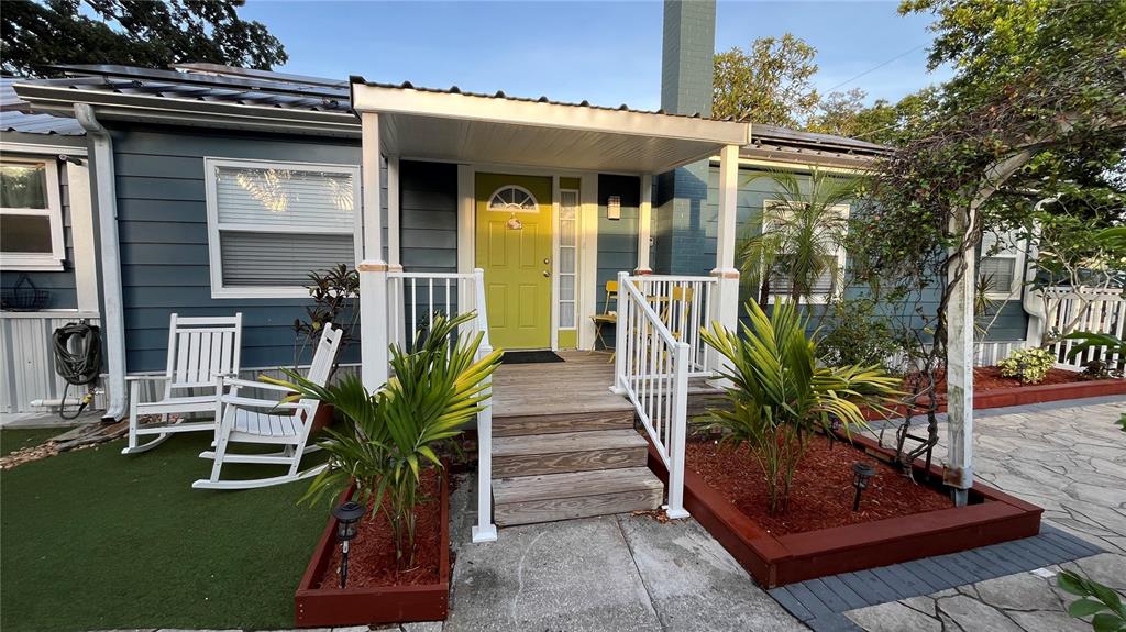 The exterior of a house features a lime green front door, white porch railings, and landscaping — 2301 W IDLEWILD AVENUE, TAMPA, FL