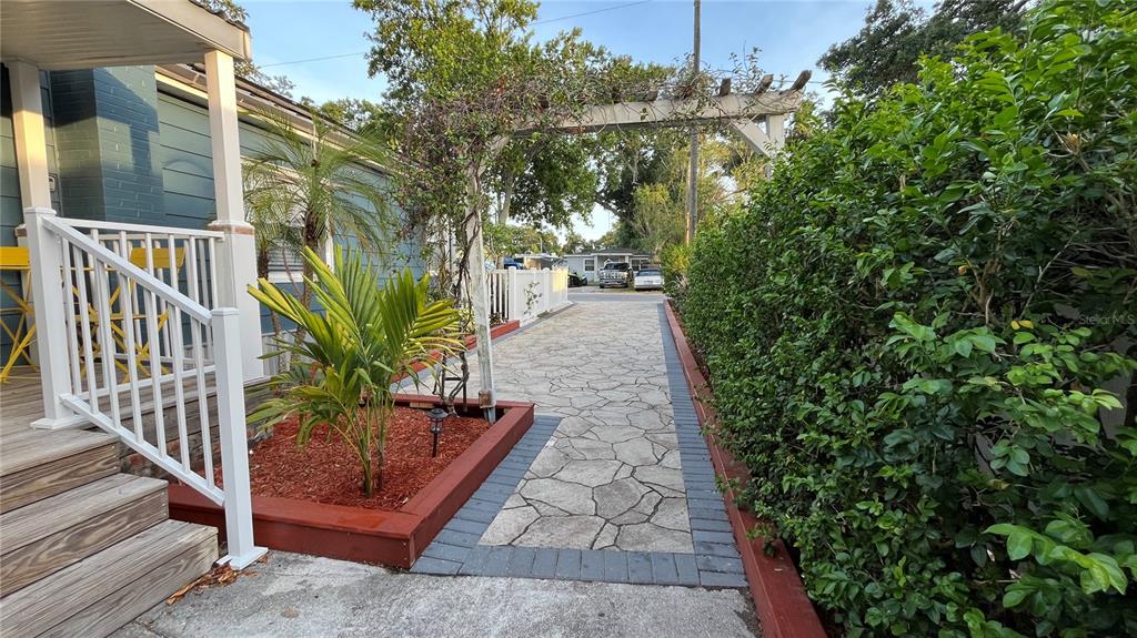 A paved walkway leads past a raised garden bed and a wooden arbor toward a street — 2301 W IDLEWILD AVENUE, TAMPA, FL